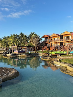 A resort with wooden buildings, a clear pool, and palm trees.