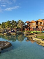 A resort with wooden buildings, a clear pool, and palm trees.