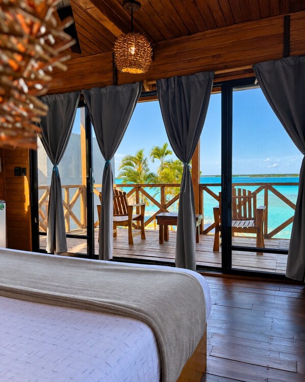 Habitación de cabaña de madera con una cama grande, terraza de madera y vista al océano.