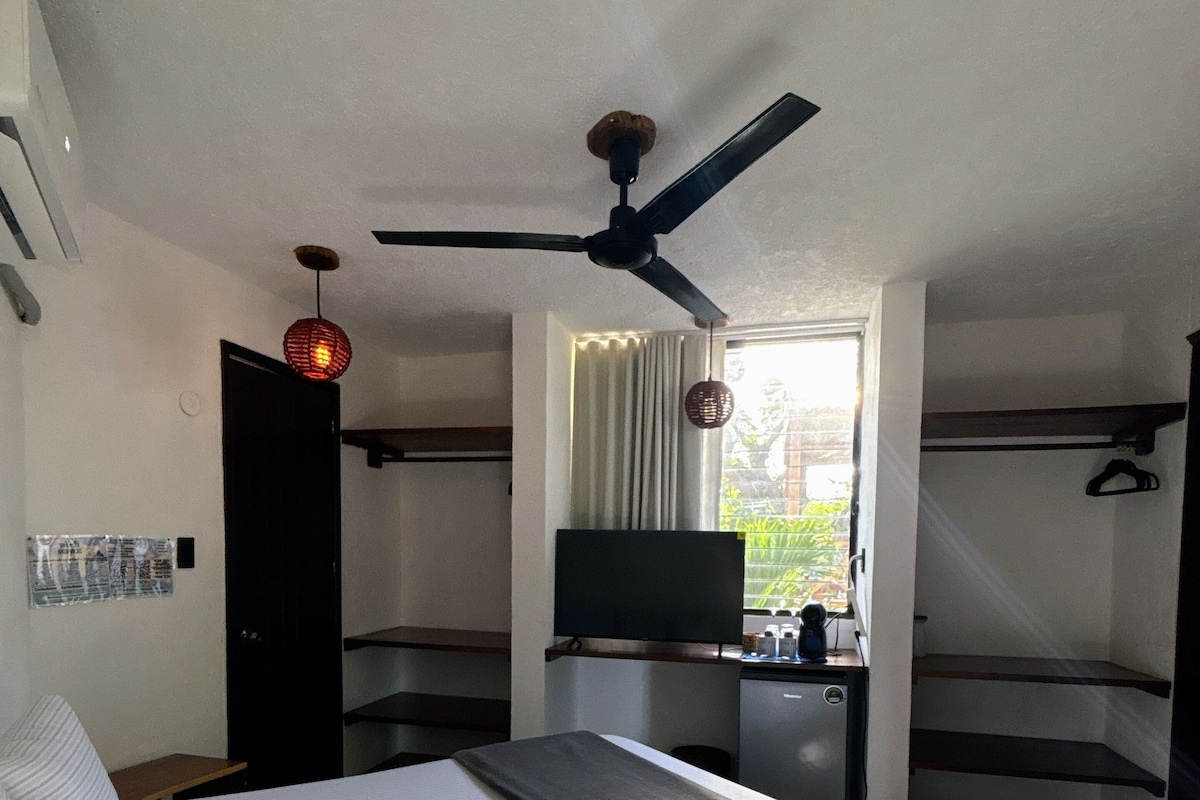 A hotel room with a bed, a ceiling fan, a television, and a window with curtains.