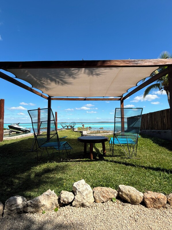 A covered outdoor seating area with a view of the ocean, a jet ski, and a wooden fence.