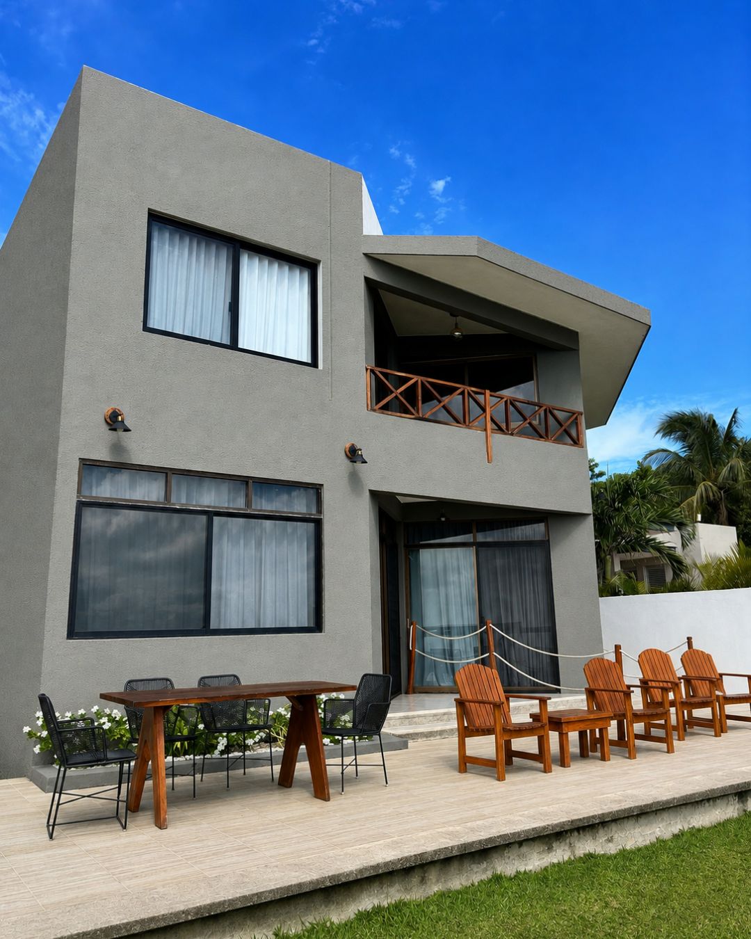 A modern two-story building with a flat roof, large windows, and a balcony with wooden railings.