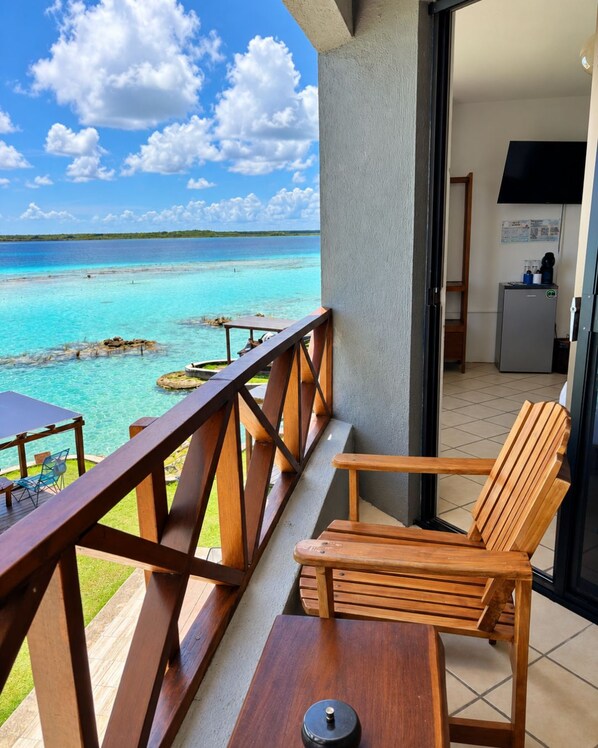 A balcony with a wooden chair and table, overlooking a turquoise sea and clear sky.