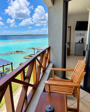 Un balcón con una silla y mesa de madera, con vista al mar turquesa y cielo despejado.
