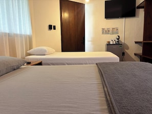A hotel room with two beds, a television, a minibar, and a door.