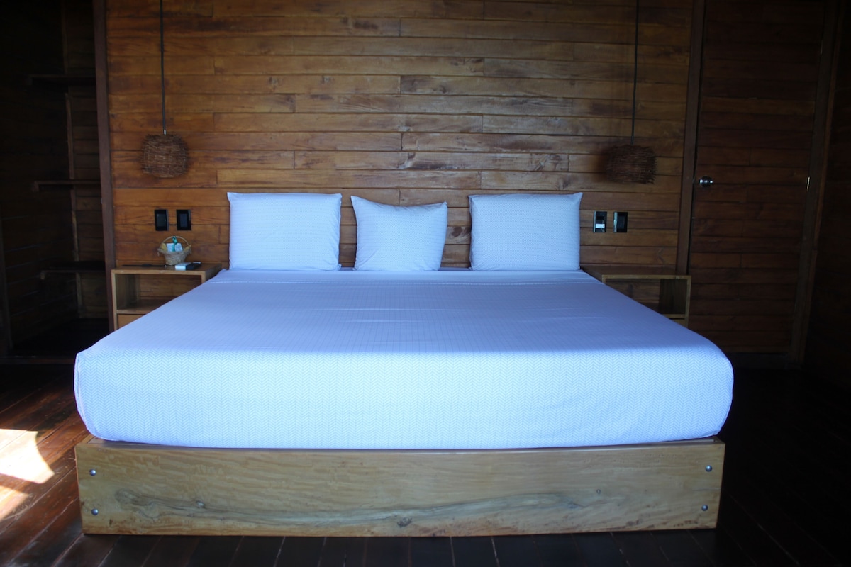 A large bed with a wooden frame and a white mattress in a room with wooden walls and a dark floor.