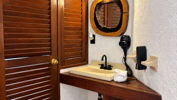 Un baño con puerta de madera, un lavabo con espejo, una toalla, una cesta y un teléfono en la pared.