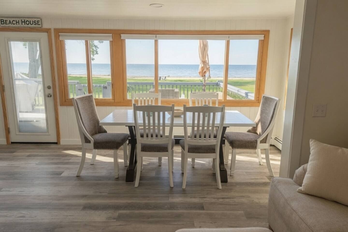 Een eetruimte met een tafel en stoelen, uitzicht op het strand, en een bord met de tekst 'Beach House'.