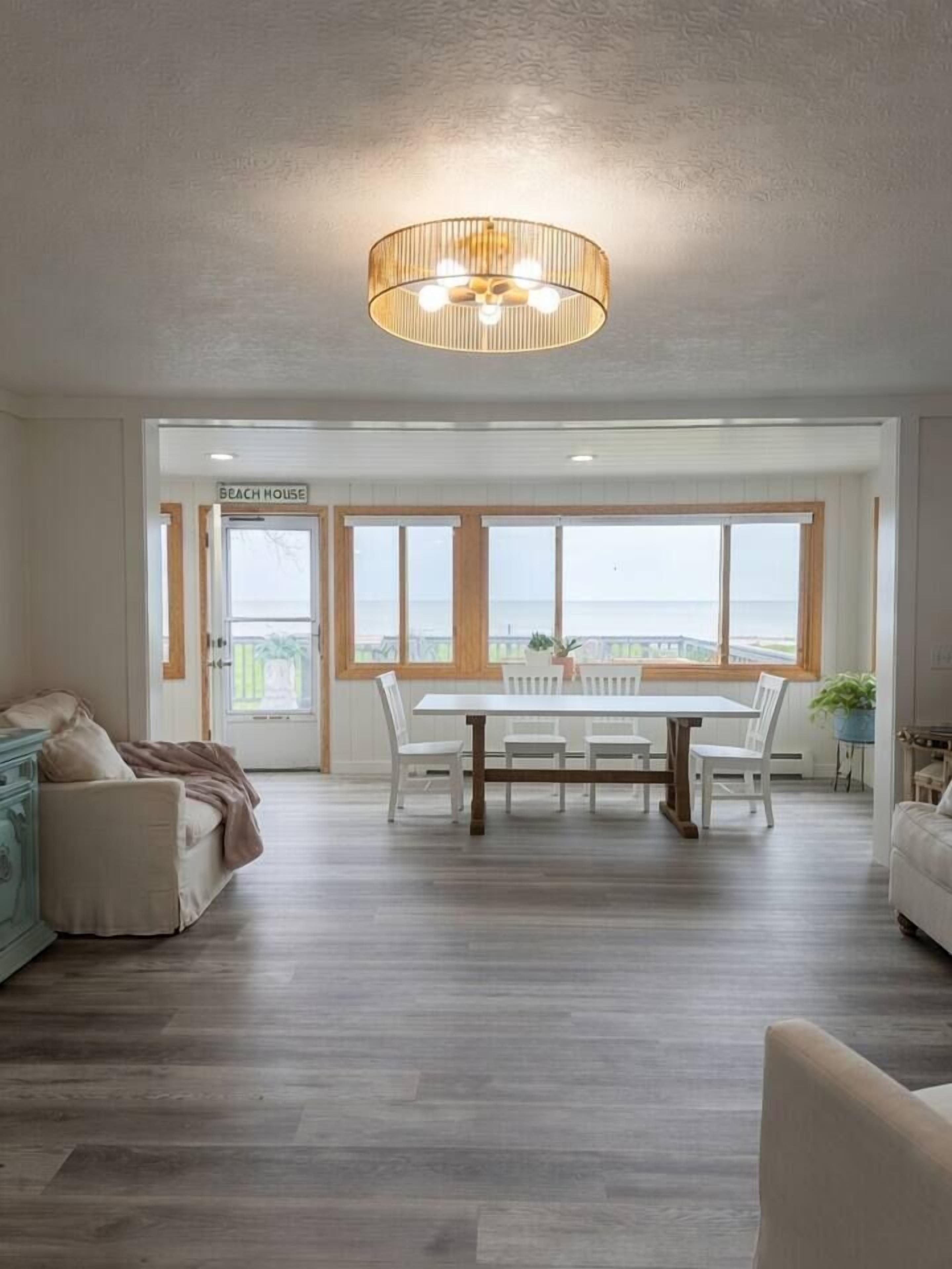 A spacious living room with a dining area, a large window with a view, and a ceiling light fixture.