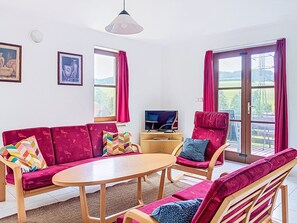 A living room with a sofa, chairs, a table, a TV, and large windows with curtains.