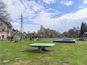 A grassy outdoor area with a swing set, a slide, and a small pool.