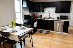 A modern kitchen with black cabinets, a stainless steel dishwasher, and a dining area with a table set for four. - Superhero Themed Family Home Near Downtown (Amarillo)