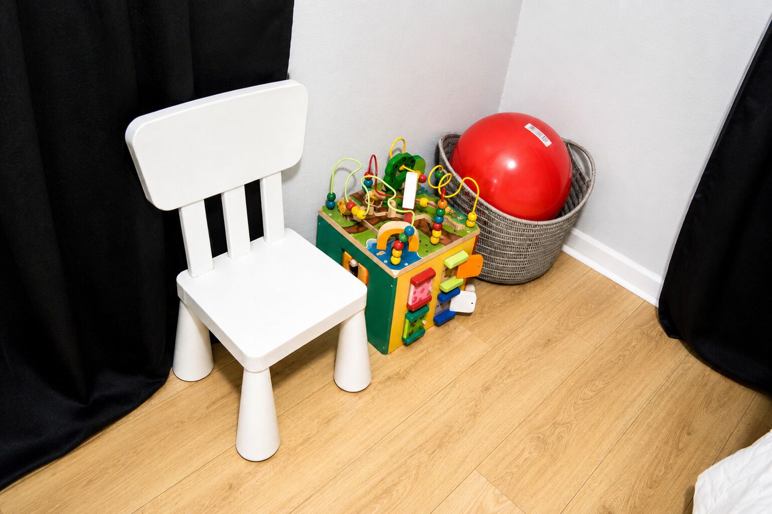 Una silla blanca, un baúl de juguete colorido y una pelota roja en una cesta.