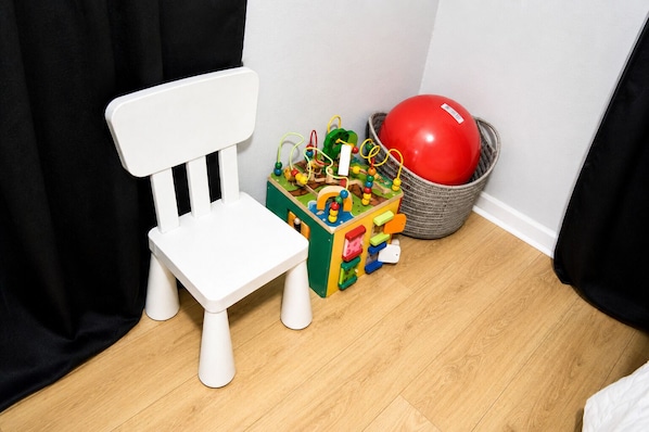 Una silla blanca, un baúl de juguete colorido y una pelota roja en una cesta.