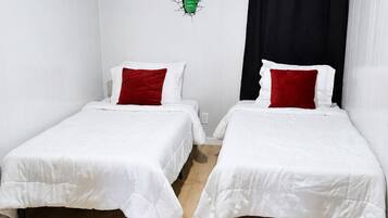 Dos camas individuales con ropa blanca y almohadas rojas, suelo de madera y cortina negra.