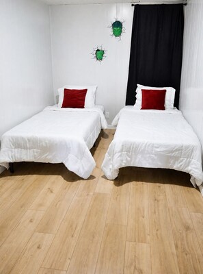 Two single beds with white bedding and red pillows, a wooden floor, and a black curtain. - Superhero Themed Family Home Near Downtown (Amarillo)