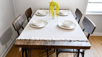 Una mesa de comedor con platos blancos, un florero transparente con flores amarillas y sillas de madera.