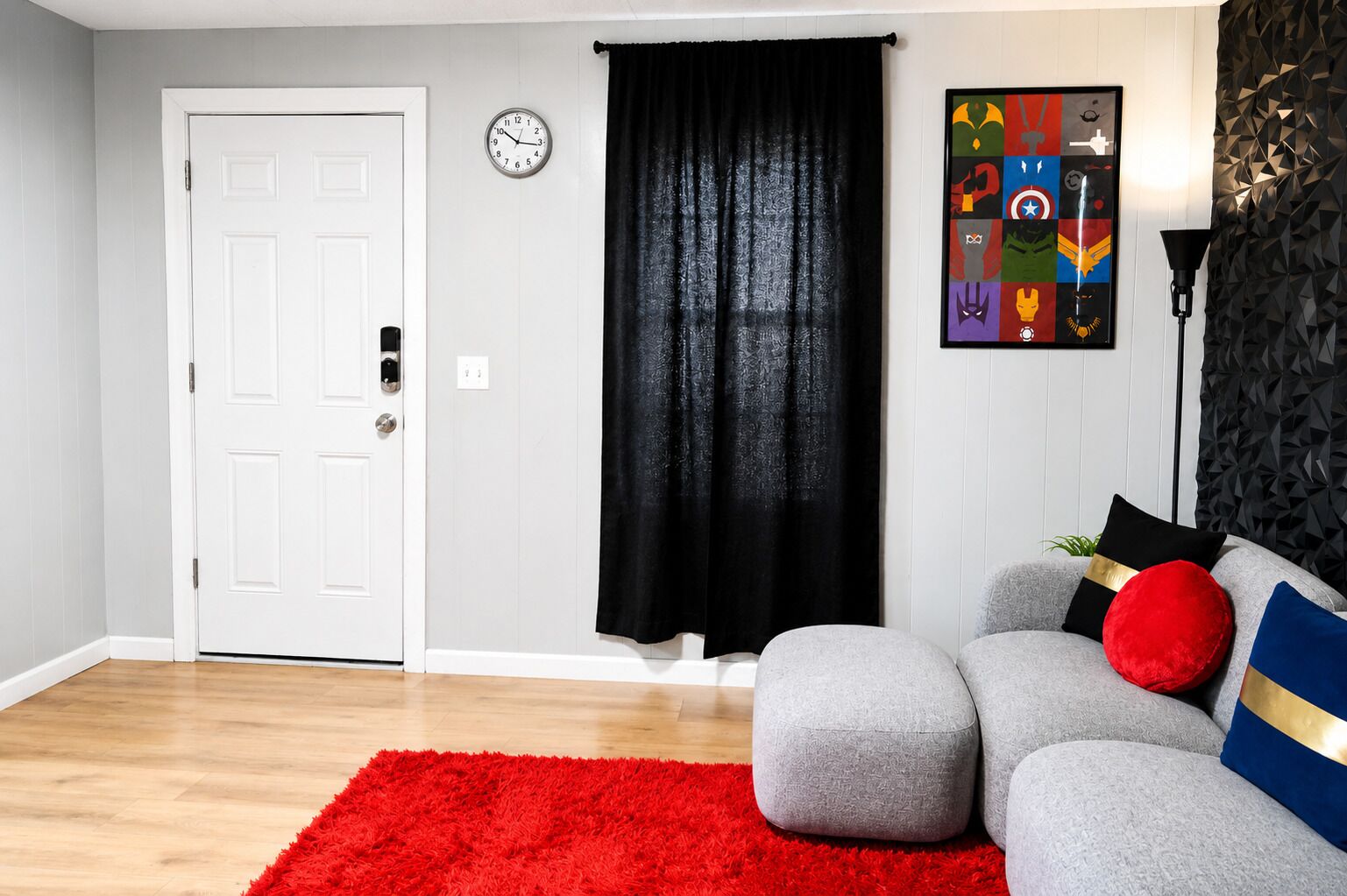 A room with a white door, a black curtain, a grey sofa with red and blue cushions, a red rug, and a wall clock.