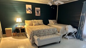 Une chambre à coucher avec un grand lit, un plus petit lit, une table de chevet avec une lampe, une chaise et un mur orné de deux tableaux encadrés.