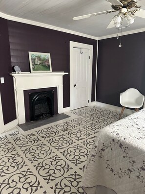 A room with a fireplace, a door, a ceiling fan, and patterned flooring.