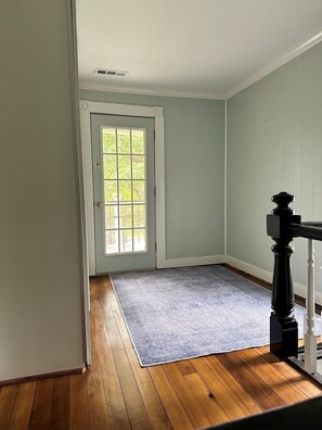A room with a wooden floor, a grey rug, a white door with a window, and a black balustrade.