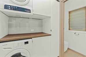 A compact laundry room with a washing machine, a dryer, and a window with blinds.