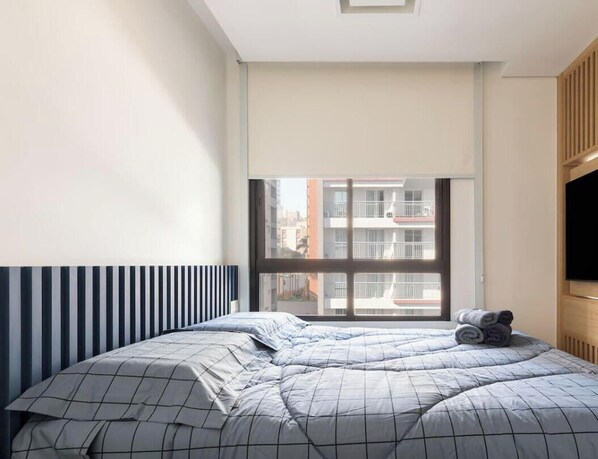 Un dormitorio con cama, ventana y televisor.
