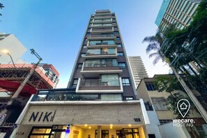 Un hotel de varios pisos con un diseño moderno, que cuenta con balcones en cada planta y una entrada visible a nivel de la calle.