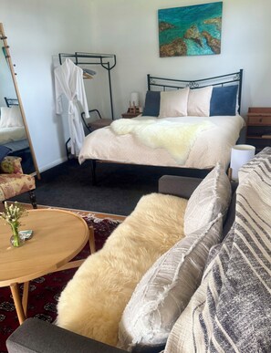A bedroom with a bed, a bedside table, a chair, a sofa, and a painting on the wall.