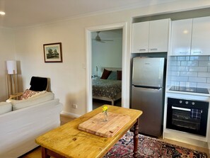 A compact living space with a kitchenette, a dining table, a sofa, and a bed in the adjacent room. - Private cottage, stunning views, amongst vines, close to beaches and wineries (Tatachilla)