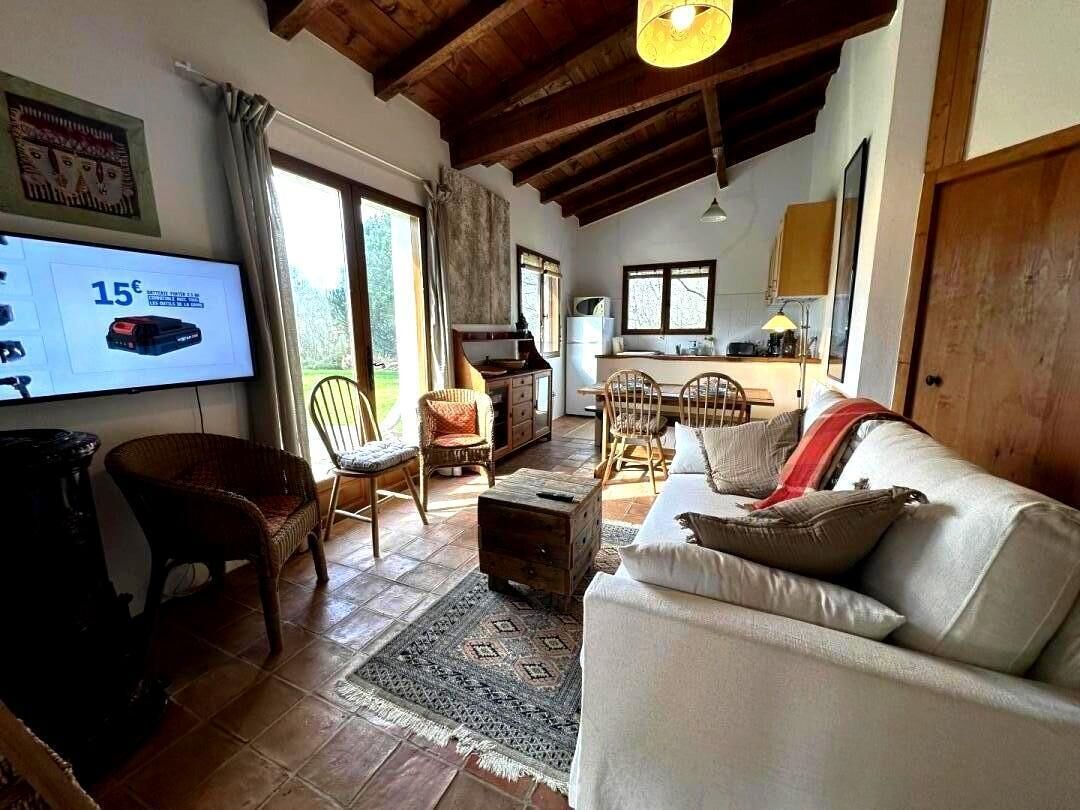 Un saló amb un sofà, cadires, televisió i una cuina al fons.