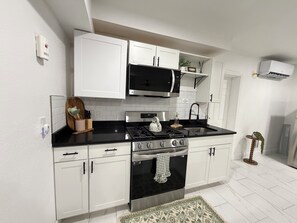 Una cocina moderna con armarios blancos, una encimera negra, una estufa de acero inoxidable y un microondas.