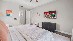 Ein Schlafzimmer mit einem Bett, einem Deckenventilator, einem an der Wand montierten Fernseher, der Netflix anzeigt, und einer Tür zu einem weiteren Raum.