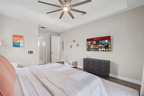 A bedroom with a bed, a ceiling fan, a wall-mounted TV displaying Netflix, and a door leading to another room. - Cape Daydream | Heated Pool, Spa & Game Room (Cape Coral)