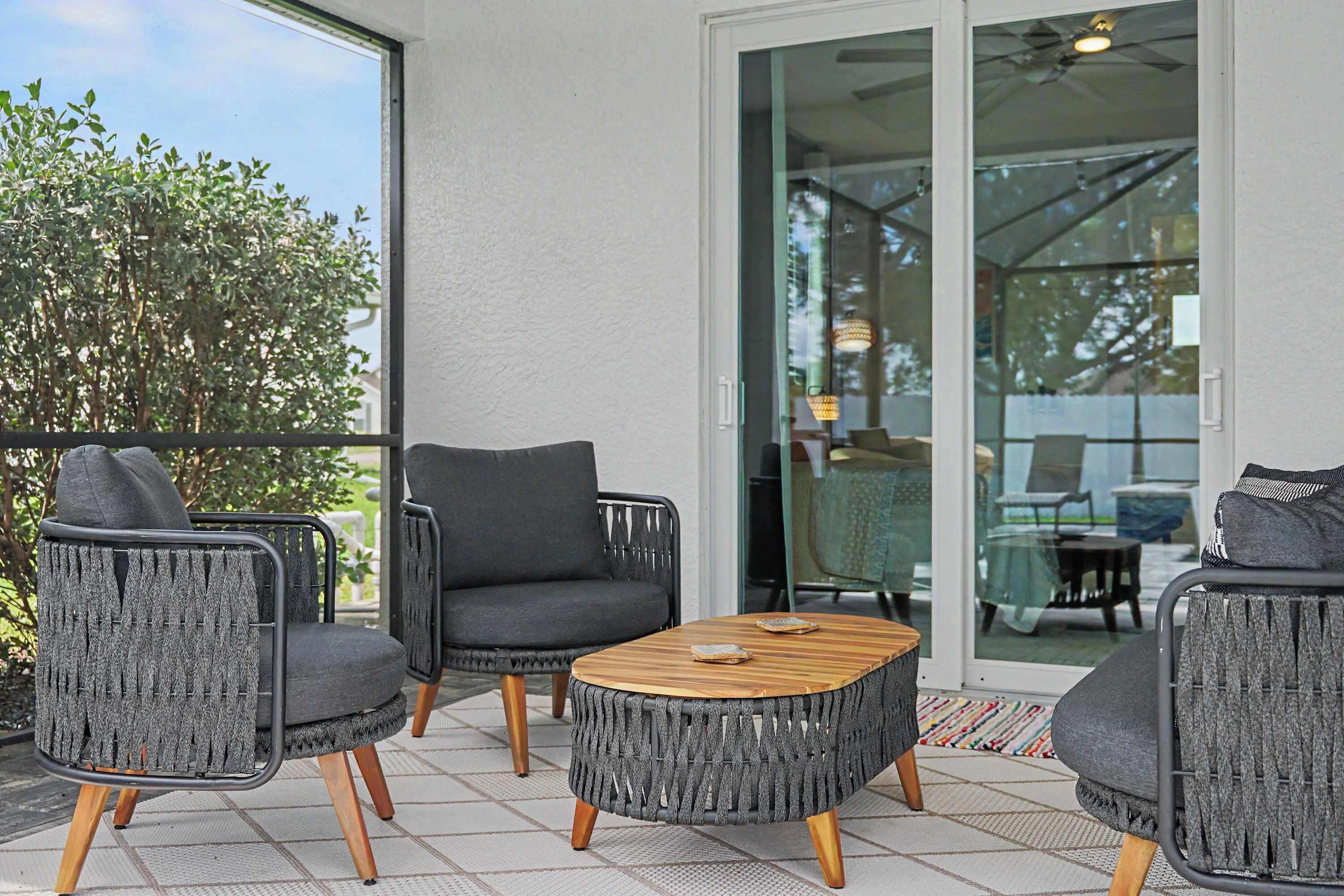 Un patio con mobiliario de mimbre, una mesa de centro de madera y una puerta de vidrio que da a un espacio interior.