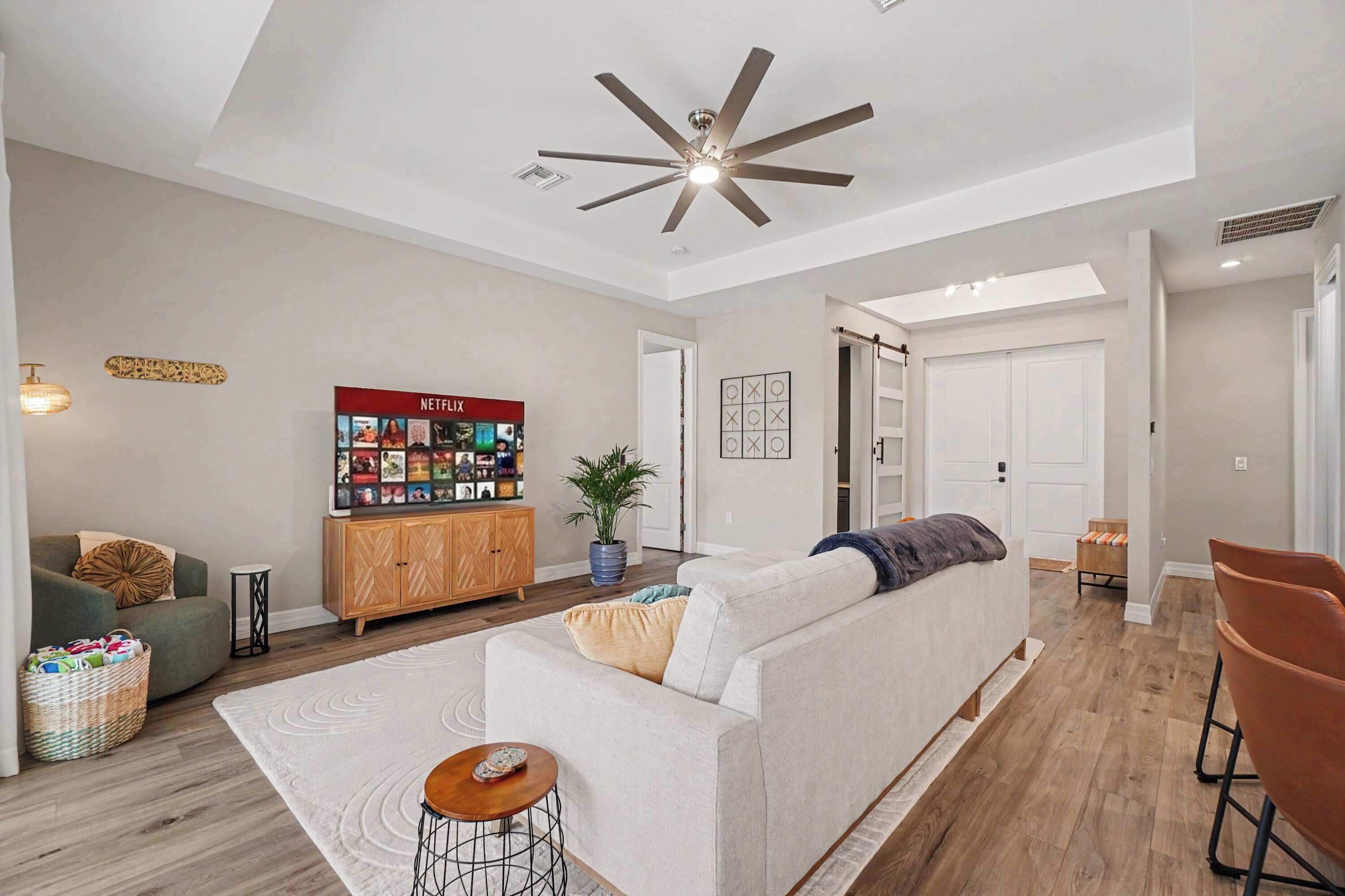 Una sala de estar moderna con un sofá, un televisor, un ventilador de techo y un mueble de madera.