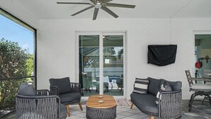 Ein überdachter Patio-Bereich mit Deckenventilator, Glastür zum Außenbereich und einer Sitzecke mit zwei Sesseln und einer Couch.