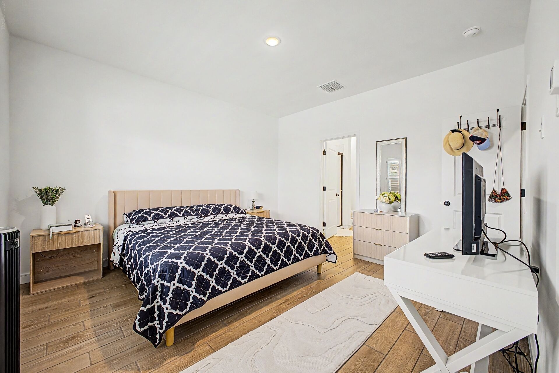 Une chambre à coucher comprenant un lit, des tables de chevet, un bureau, un miroir et une armoire.