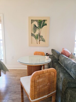A room with a round glass table, wicker chairs, a grey sofa, and a framed plant artwork on the wall. - The Coral Palm - Modern, Coastal Boutique Retreat (Inlet Beach)