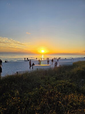 Een strandgezicht met mensen die langs het water lopen en staan tijdens de zonsondergang.