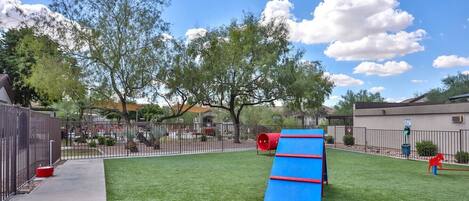 A fenced backyard with artificial grass, a blue and red slide, and a red tunnel.