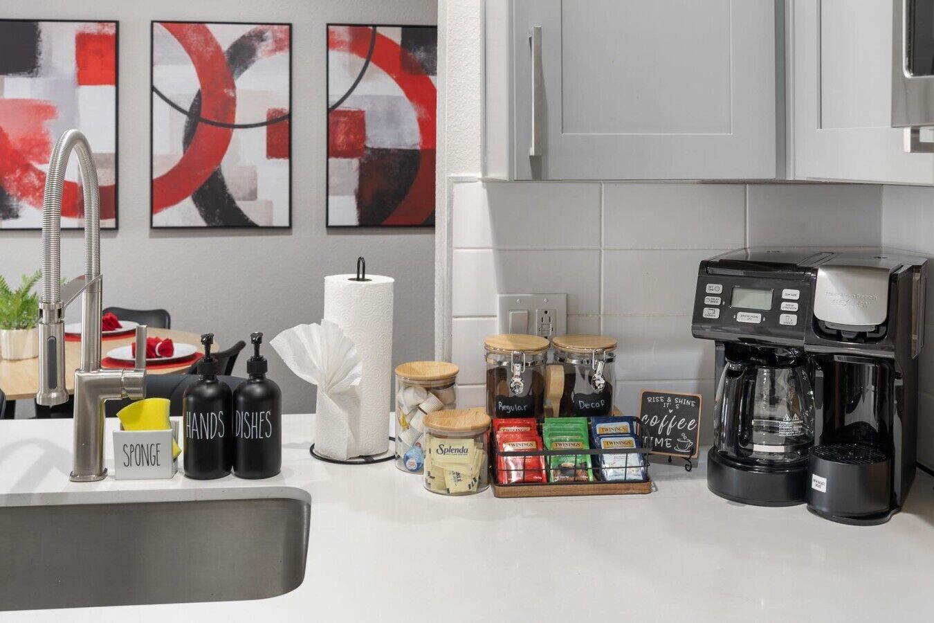 A modern kitchen with a coffee maker, jars of spices, and a sponge holder.