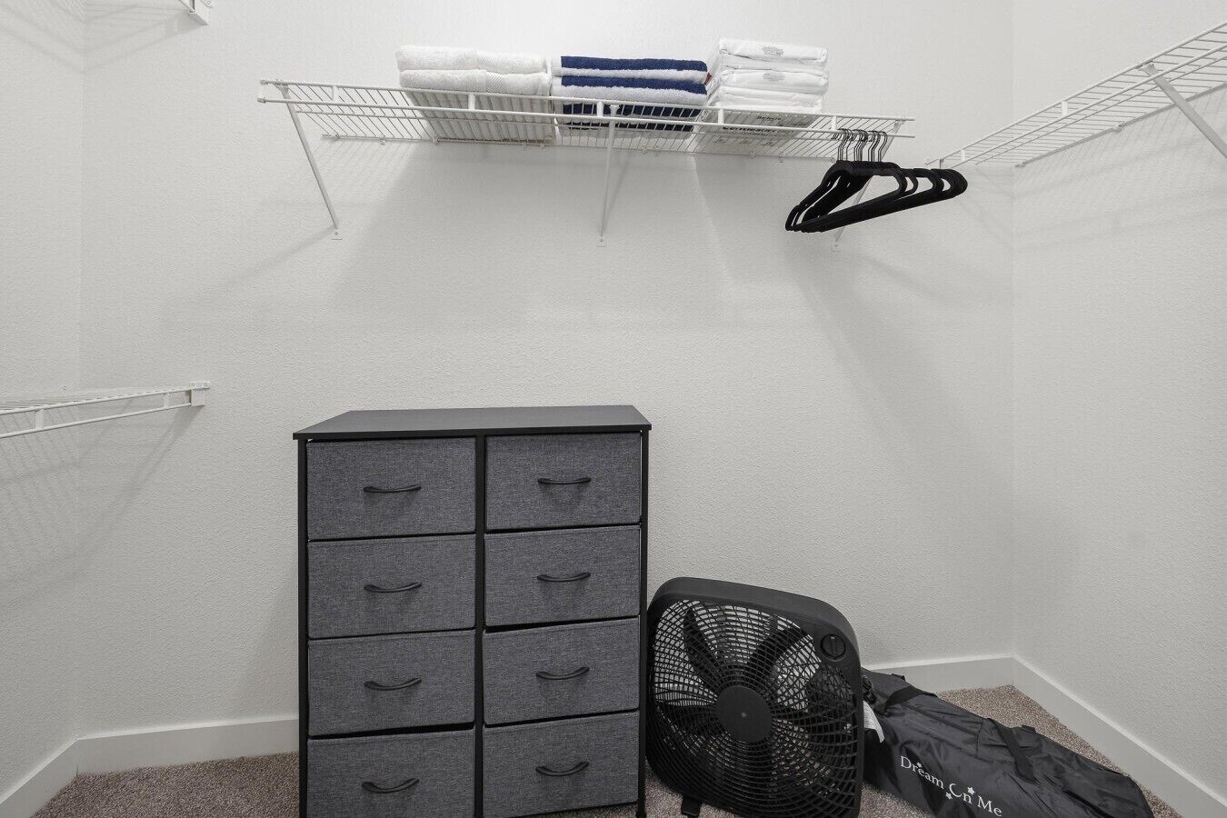 A small, enclosed room with a metal shelf holding folded towels and a black fan.