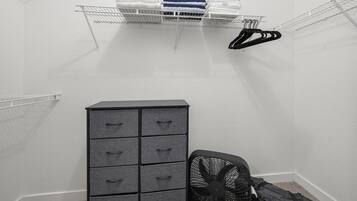 A small, enclosed room with a metal shelf holding folded towels and a black fan.