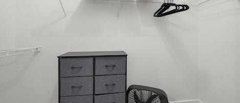 A small, enclosed room with a metal shelf holding folded towels and a black fan.