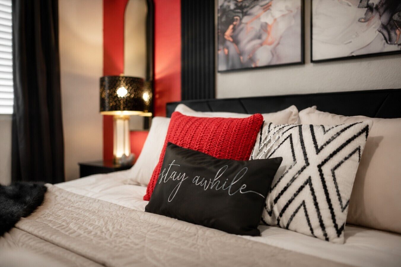 A bed with a black pillow with white text, a red pillow, and a black and white patterned pillow.