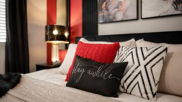 A bed with a black pillow with white text, a red pillow, and a black and white patterned pillow.
