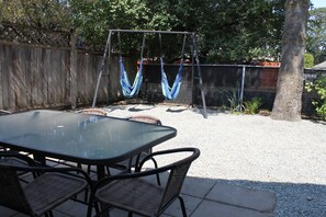 A patio with a glass table and wicker chairs, a swing set, and a wooden fence. - SuiteHart Hideaway: 2 King Beds and 2 Full Baths (Victoria)