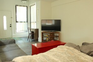 A living room with a television on a wooden stand, a red coffee table, and a sofa. - SuiteHart Hideaway: 2 King Beds and 2 Full Baths (Victoria)