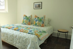 A bedroom with a bed, pillows, a small stool, a framed picture on the wall, and a window. - SuiteHart Hideaway: 2 King Beds and 2 Full Baths (Victoria)